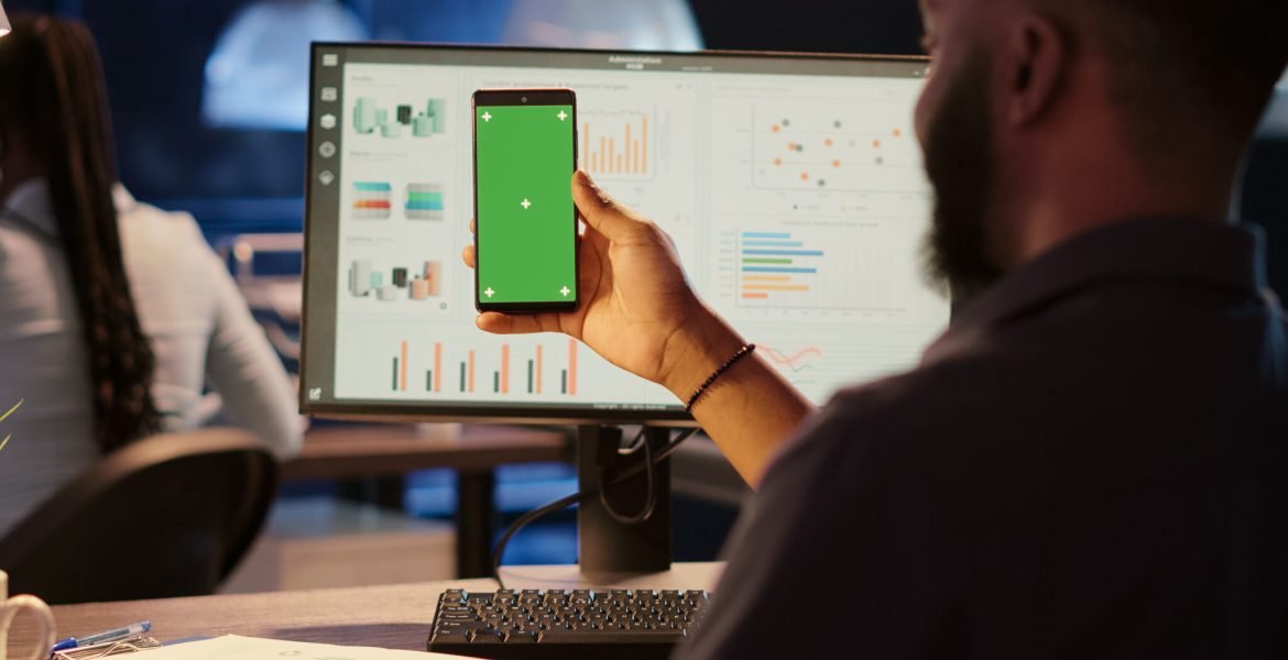 Business man looking at greenscreen display on mobile phone Business man looking at greenscreen display on mobile phone, working in office at night. Using isolated chroma key background with blank copyspace and mockup template on smartphone.